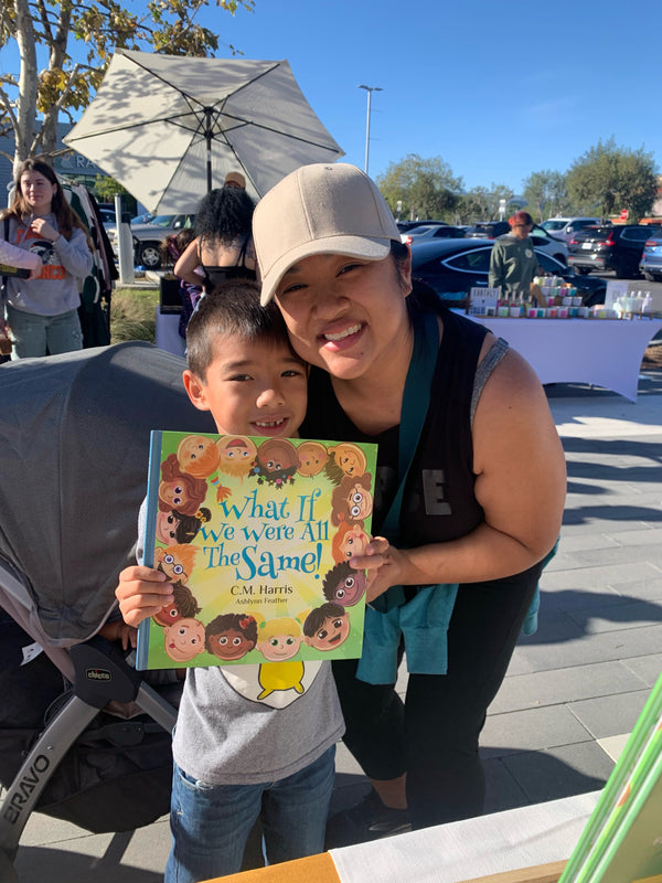 Woman and child holding a book titled 'What If We Were All The Same?' at an outdoor event.